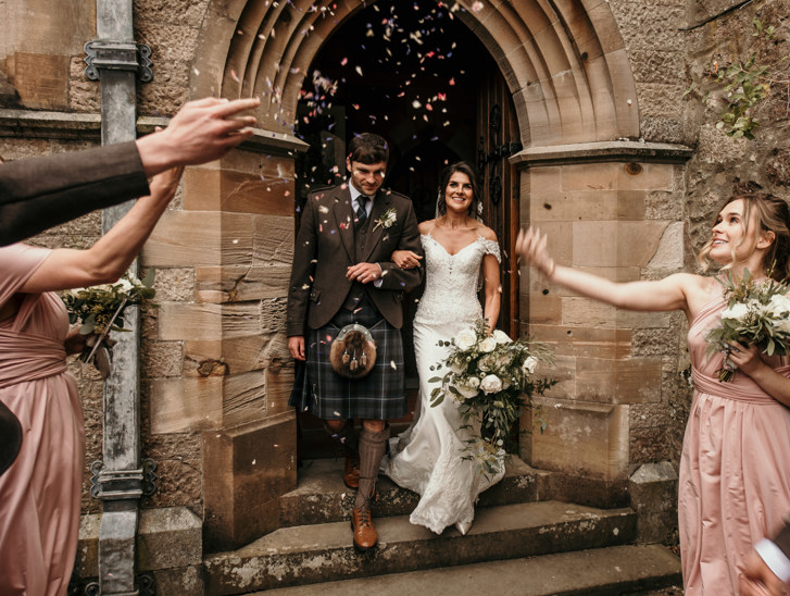 groom and bride walking out of church doorway with bridesmaids throwing confetti